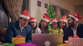 Cheerful happy smiling modern well dressed Indian Asian family members wearing Santa caps sitting together interacting or talking while shopping online on a laptop during During Christmas eve holidays