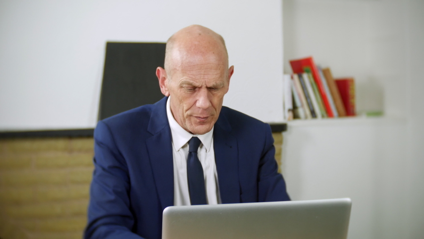 A tired mature businessman is working on his laptop in his home office. The man looks stressed from working hard. | Shutterstock HD Video #1097504085