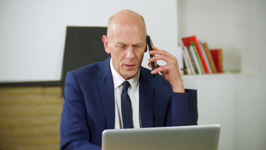 An angry mature businessman is talking on the phone in his home office. He is speaking to customer services and is frustrated and upset. | Shutterstock HD Video #1097504087