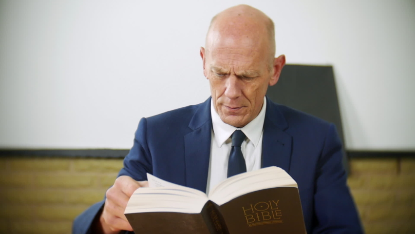 A professional businessman is reading the Holy Bible at home. The religious man is exploring his spirituality. Her reads and turns the pages deep in thought. | Shutterstock HD Video #1097504131