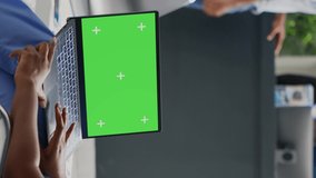 Vertical video: Nurse holding laptop with greenscreen display in waiting room, using isolated mockup template in hospital reception. Young woman working with blank chroma key and copyspace. Tripod