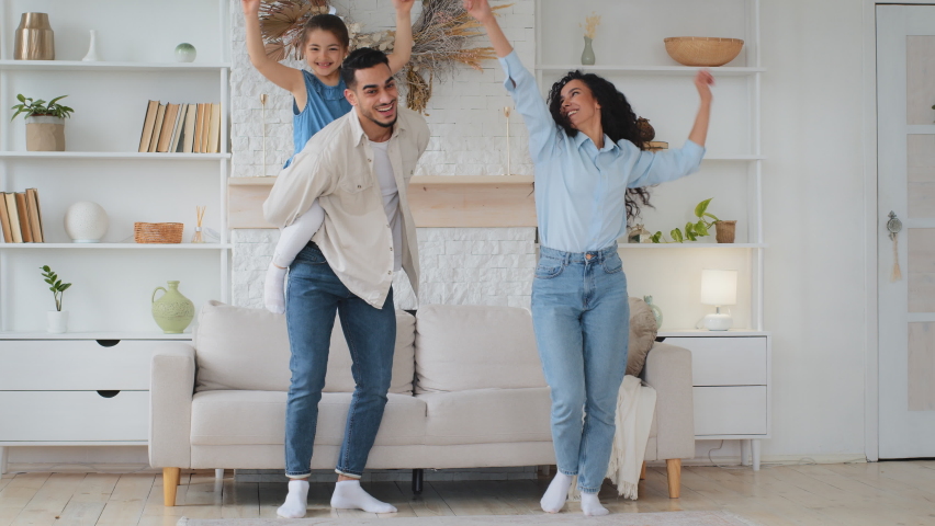 Hispanic multiethnic multiracial family dancing at home living room with little schoolgirl daughter sitting piggyback on father back pretend airplane pilot fly game celebrating enjoying music dance Royalty-Free Stock Footage #1097507883