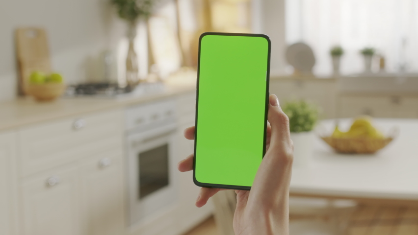 Handheld Camera: Back View of Woman at Kitchen Room Using Phone With Green Mock-up Screen Chroma Key Without Track Points Surfing Internet Watching Content Videos Blogs. Swipe Up and Tap Center Royalty-Free Stock Footage #1097509793