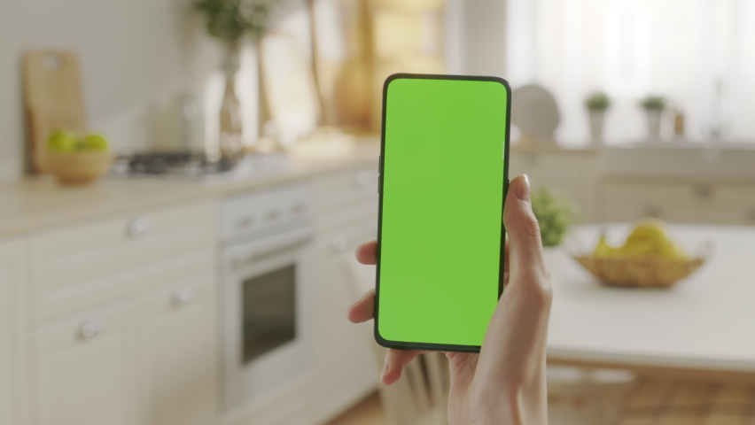Handheld Camera: Point of View of Woman on Kitchen Room Holding Chroma Key Green Screen Smartphone Watching Content Without Touching or Swiping. Female Using Mobile Phone, Browsing Internet, Watching Royalty-Free Stock Footage #1097509859