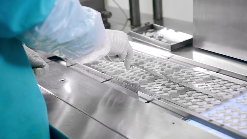 Factory worker is replacing some capsule pills on the conveyor