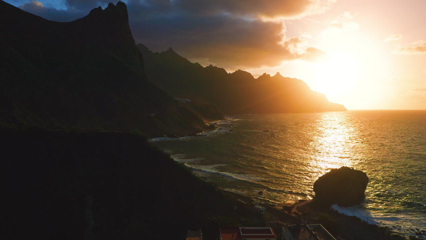 Colorful sunset light over ocean water, waves crash on rocky mountain beachfront. Aerial sun set above cliffs silhouette. Tropic nature seascape. Paradise island Tenerife Spain. Cinematic drone shot. | Shutterstock HD Video #1097519749