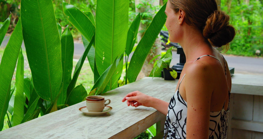 Girl smells and drinking hot morning Balinese coffee enjoying green tropical garden nature. Side view of lonely travel woman in Bali Island Nusa Penida Indonesia. Outdoor. | Shutterstock HD Video #1097519761