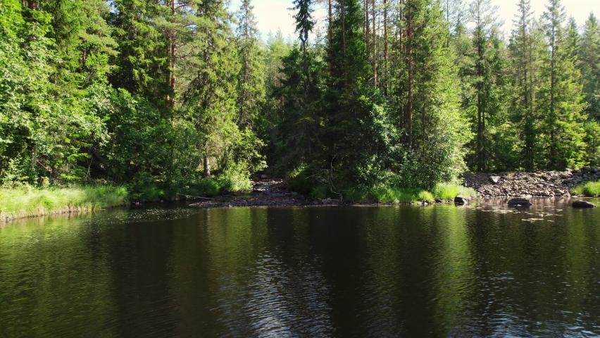 View of a creek in the shadows flowing into a lake. Low angle view arc shot, sun shines on the woods in Scandinavian nature. Stream in the forest on a sunny day in the nature of Sweden Summer season Royalty-Free Stock Footage #1097521481