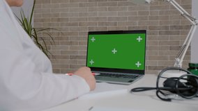 Medical worker studying online on green screen chroma key laptop. Doctor passing a training online using laptop.