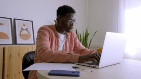 Young African American man typing on laptop, concentrated working from home. 4k video.