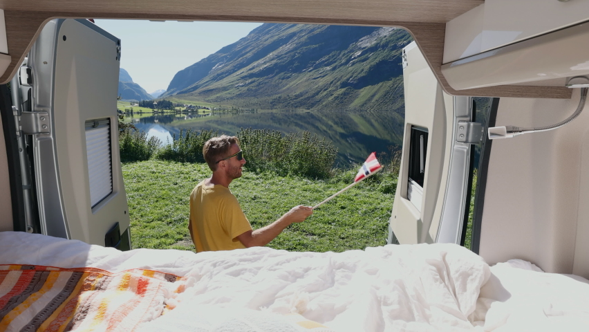 Man waving Norwegian flag from his camper van. Traveller camping in Norway 