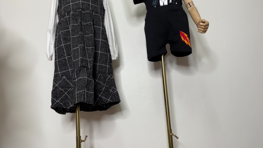 Child mannequin wear shirt, pants and dress on gold pole holding number card with white wall background | Shutterstock HD Video #1097527277