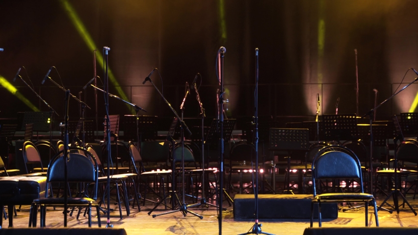 Concert light. Stage lighting background. An empty stage and a hall without people. There are a lot of empty chairs and microphones on the stage for musicians.