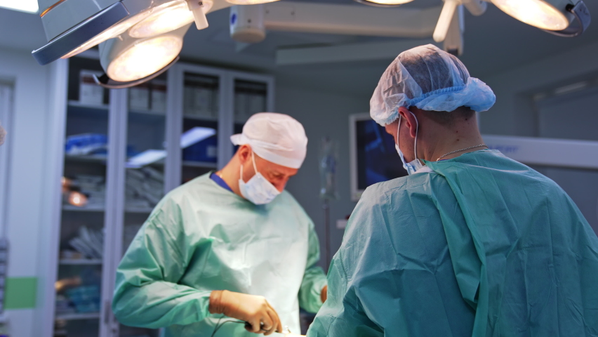 Plastic surgery conducted by a couple of surgeons. Nurse and anesthesiologist standing at the feet of the patient. Modern operational room backdrop. Royalty-Free Stock Footage #1097537537