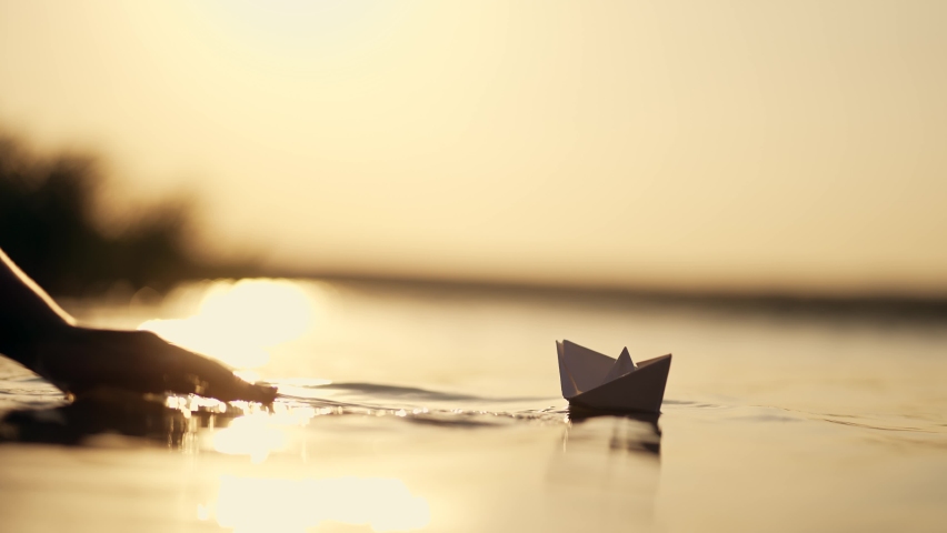 Large paper boat is launched by girl on water on shore. Beautiful landscape background. Paper boat on water. Launch boat. Summer travel by sea. girl's hand is holding boat. Beautiful beach background.