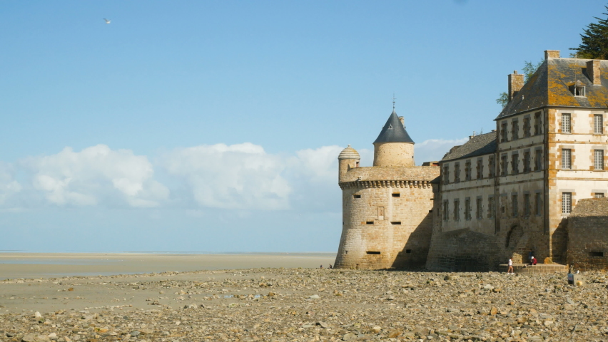 The medieval walls made of stone of Mont Saint Michel, Normandy, France, on the coastline of Normandy during low tide. Blue sky on the background.