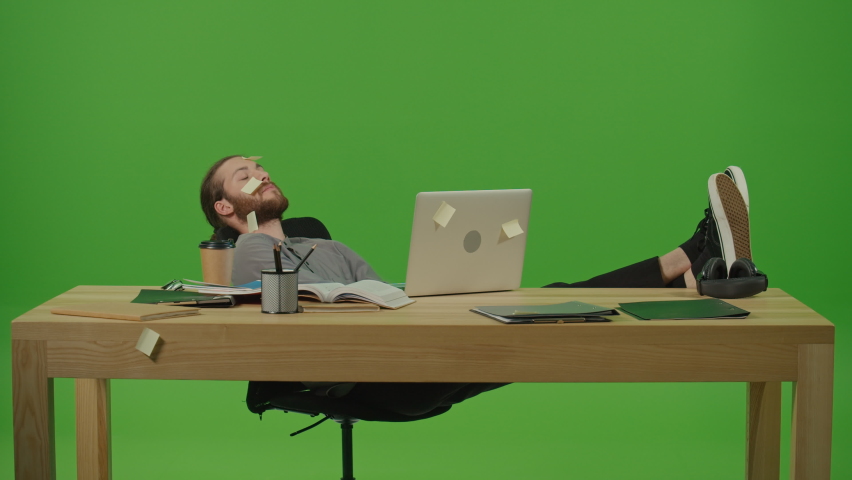 Tired Bearded Student with Legs on Table and Laptop Trying to Sleep after Hard Work Study Day.It is a Lot of Stickers on His Face,Laptop,and Table on Green Screen,Chroma Key.Computer Overwork Concept