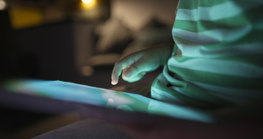 Closeup kid boy using digital tablet technology device lying in living room Small child hold pad computer surfing internet play game at home. Children tech addiction concept