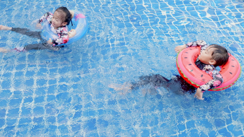Asian two children little girls and boy playing in outdoor swimming pool on inflatable toy ring, Happy brother and sister playing in the pool tropical resort during family summer vacation