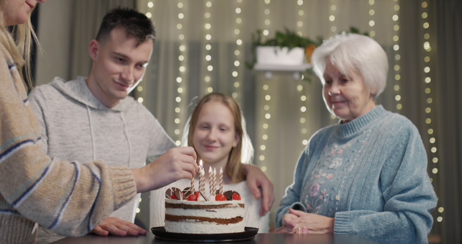 Mom lights candles on her daughter's birthday cake. Family members standing by | Shutterstock HD Video #1097553741