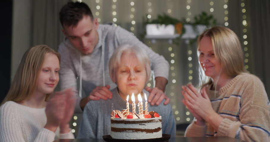 An elderly lady blows out candles on a birthday cake, her family is nearby. Merry birthday | Shutterstock HD Video #1097553749