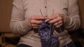 The video shows how a woman knits a woolen sock with metal knitting needles.
