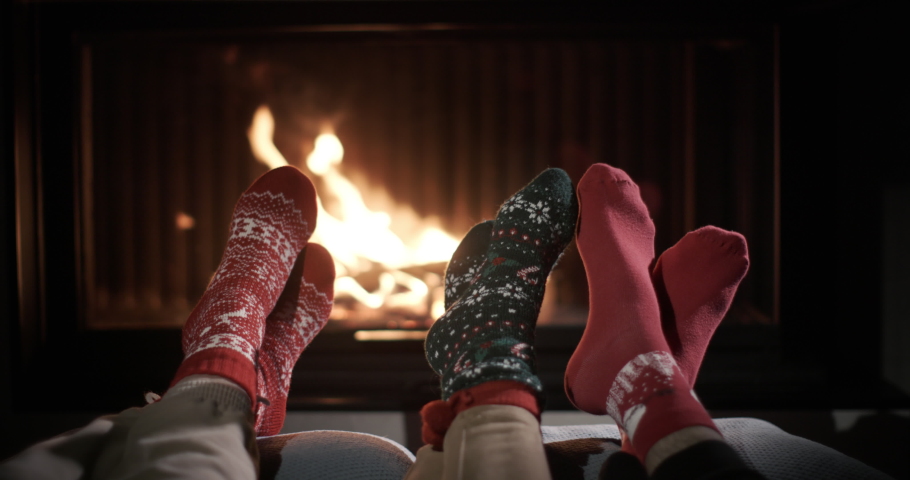 Three people are warming their feet by the fireplace. Niogs are wearing bright New Year's socks | Shutterstock HD Video #1097557047