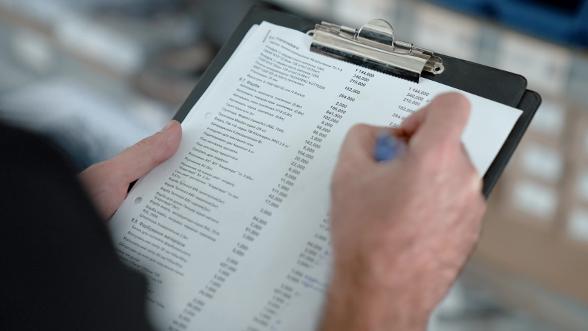 Hand with a pen makes notes on paper on a clipboard. Warehouse worker. | Shutterstock HD Video #1097560559