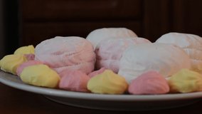 In the video, sweet cakes of different colors, soft marshmallows and sweet meringue lie on a plate. The plate is rotating.