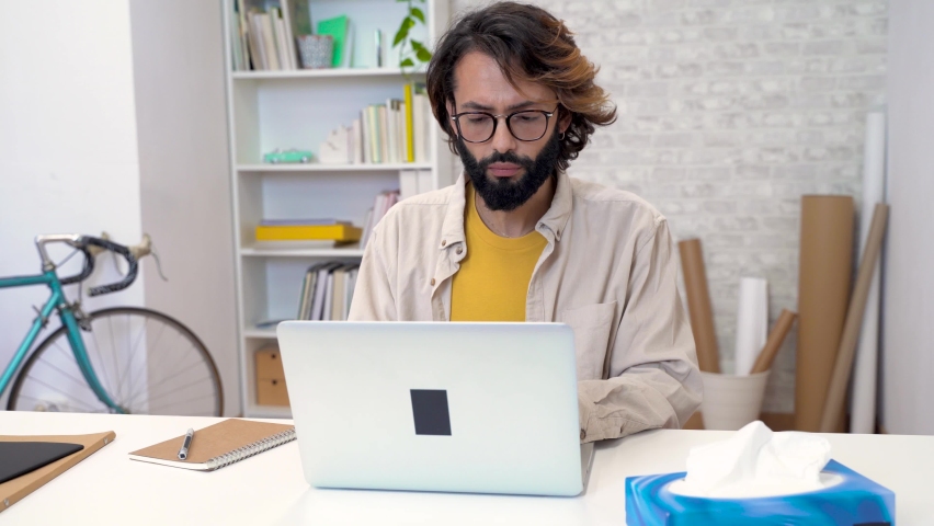 Unhealthy man working on computer, feeling sick first flu symptoms, allergic runny nose using paper tissues | Shutterstock HD Video #1097561761