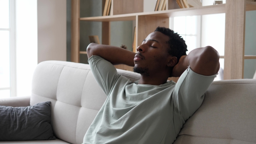 Young, relaxed African-American men is resting on the couch with her eyes closed after a hard day's work. The concept of rest and tranquility. Royalty-Free Stock Footage #1097566435