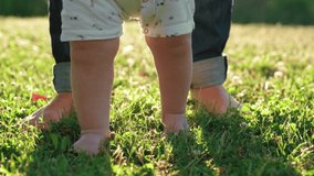 Walking children's bare feet on a green lawn close-up. Child  learns to take the first steps.  Baby learns to walk with the help of his mother on a green grass in the park. Slow motion 4k video.