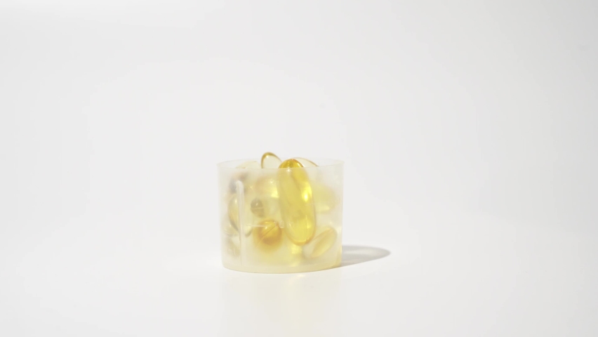 Close-up Female Hand putting transparent golden pills into measuring cup over white background | Shutterstock HD Video #1097573629