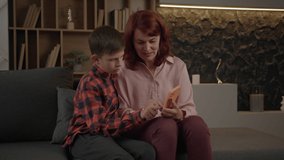 Mother learning her autistic son how to use smartphone sitting on the sofa at home. Boy with autism using mobile phone with mom's help. - Powered by Shutterstock - Get 15% off with code: PIKWIZARD15