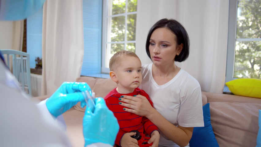 Doctor take swab from mother and toddler son visiting at home. Young woman with sick baby son have pediatrician in living room. Realtime.  | Shutterstock HD Video #1097577943
