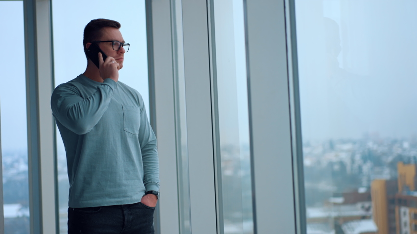 Caucasian fit man standing at the panoramic window with hand in the pocket. Businessman having phone conversation looking at the window. | Shutterstock HD Video #1097578255