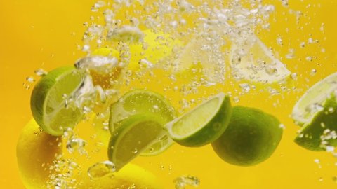 Стоковое видео: Close-up of falling sliced limes and lemons into the water on orange background, making a cocktail of citrus fruits, drinking cold lemonade, shooting of carbonated water with sliced fruits. 