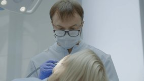 Male dentist drills tooth to female patient in dental chair. Close-up. Slow motion