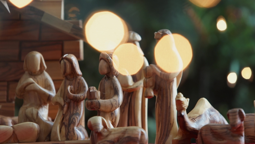 Camera dolly left across olive wood creche nativity with hand placing baby Jesus into manger