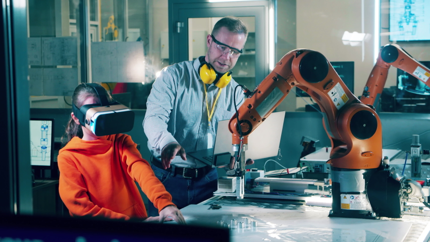 A girl in VR-glasses and an engineer are operating a robotic arm