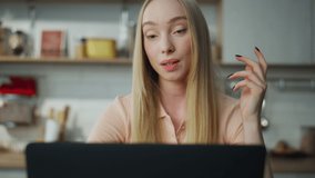Cheerful woman manager finishing online meeting waving hand on web camera sitting home kitchen close up. Blond attractive girl saying goodbye at video call. Pretty lady working remotely with laptop.