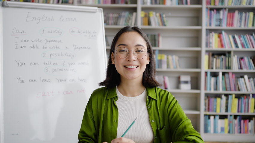 Young Asian woman explains topic at English classes. Positive female teacher in glasses points to notes on whiteboard and tells new material emotionally Royalty-Free Stock Footage #1097589693