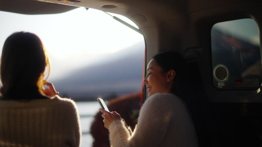 Happy Asian woman friends relax and enjoy outdoor lifestyle using mobile phone with internet while driving car travel Kawaguchi lake and Mt Fuji covered in snow on autumn road trip holiday vacation. Royalty-Free Stock Footage #1097590533