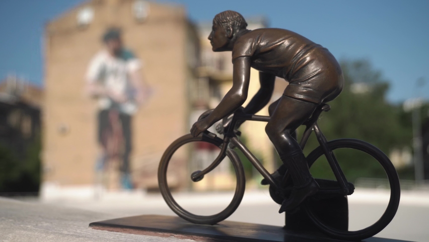 A small figurine of a cyclist on a cycle track, in the center of a big city. Against the backdrop of houses, with drawn, underground graffiti. Kyiv. Ukraine. day, summer
