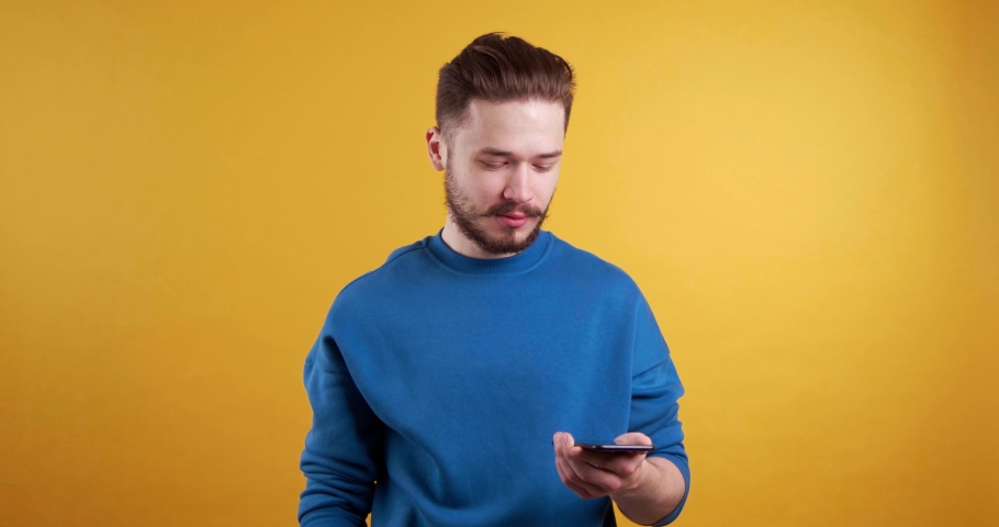Young man full of hope becoming sad about information in mobile phone. Yellow background | Shutterstock HD Video #1097599615