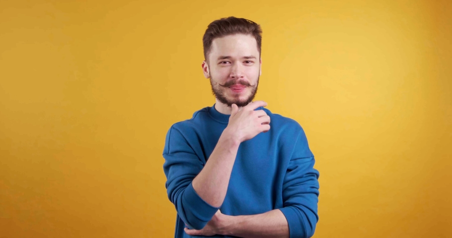 Flirting. Young man looking at camera, giving assessing look and winking. Yellow background | Shutterstock HD Video #1097599687