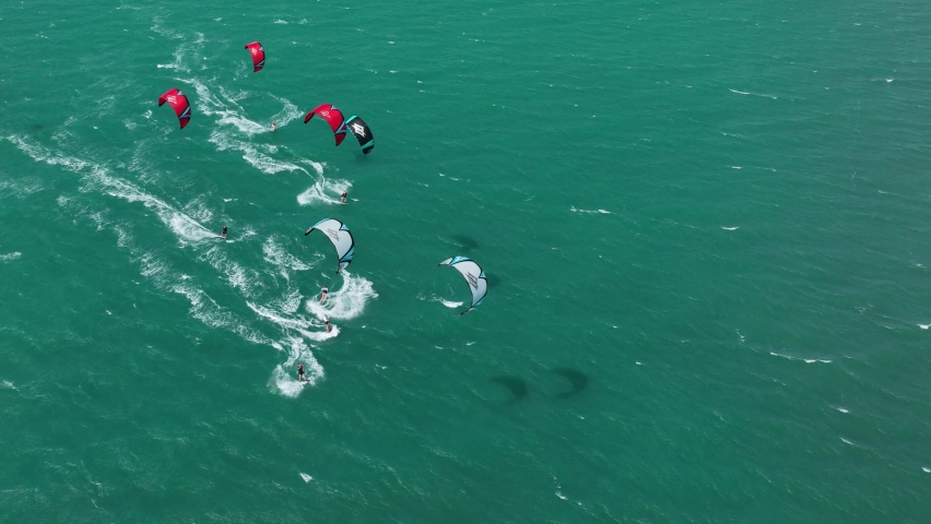 Wide aerial shot of a group of kitesurfers racing across the ocean in the high wind on light green sea, Northern Brazil Royalty-Free Stock Footage #1097611089