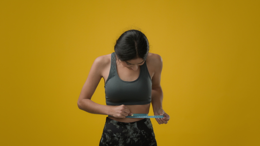 Indian strong slim sport woman girl athlete lady with measure tape measuring waist size in studio yellow background happy rejoice with successful achieve good healthy body shape loose weight training Royalty-Free Stock Footage #1097615421