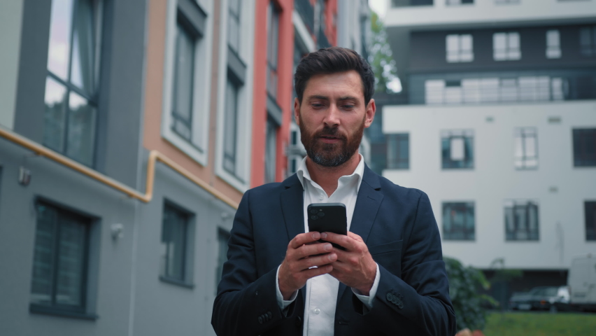 Caucasian adult 40s man happy smiling businessman boss work on modern smartphone outdoors walking city look at mobile phone navigation chatting online read message use banking app e-business concept | Shutterstock HD Video #1097615465