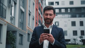 Caucasian adult 40s man happy smiling businessman boss work on modern smartphone outdoors walking city look at mobile phone navigation chatting online read message use banking app e-business concept - Powered by Shutterstock - Get 15% off with code: PIKWIZARD15